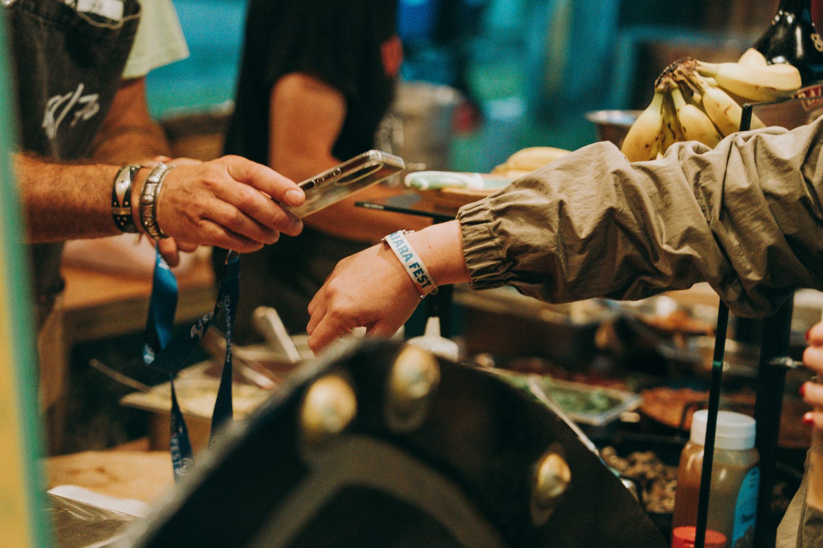 A festival-goer tapping their phone to pay, an NFC event wristband visible on their wrist